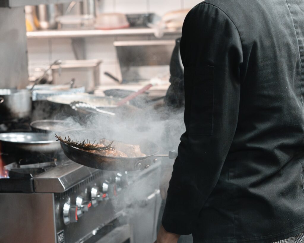 A chef at the range with a pan over the flame in The Ivy kitchen